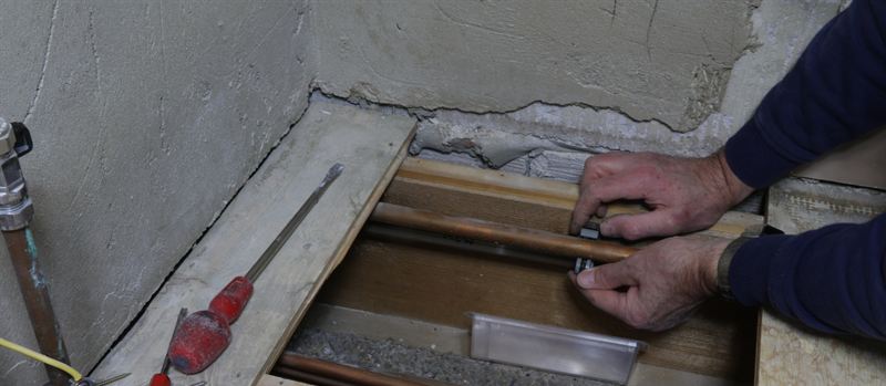 Engineer fitting a connector to copper gas pipework laid beneath floor level